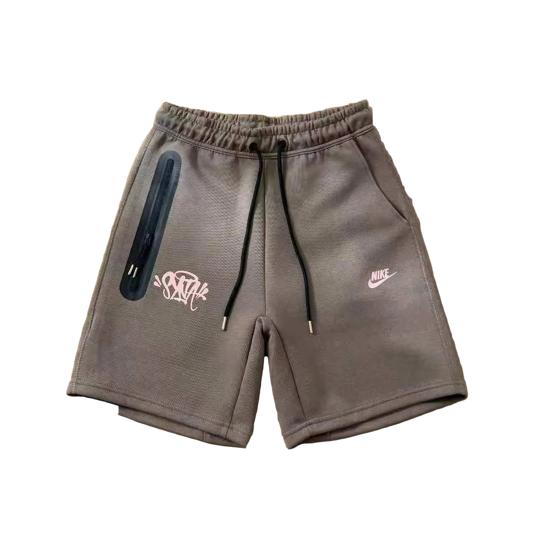 Gray Nike athletic shorts with a black drawstring, a vertical black zip pocket on the left leg, and pink graphic logos, laid flat on a tan cardboard background.