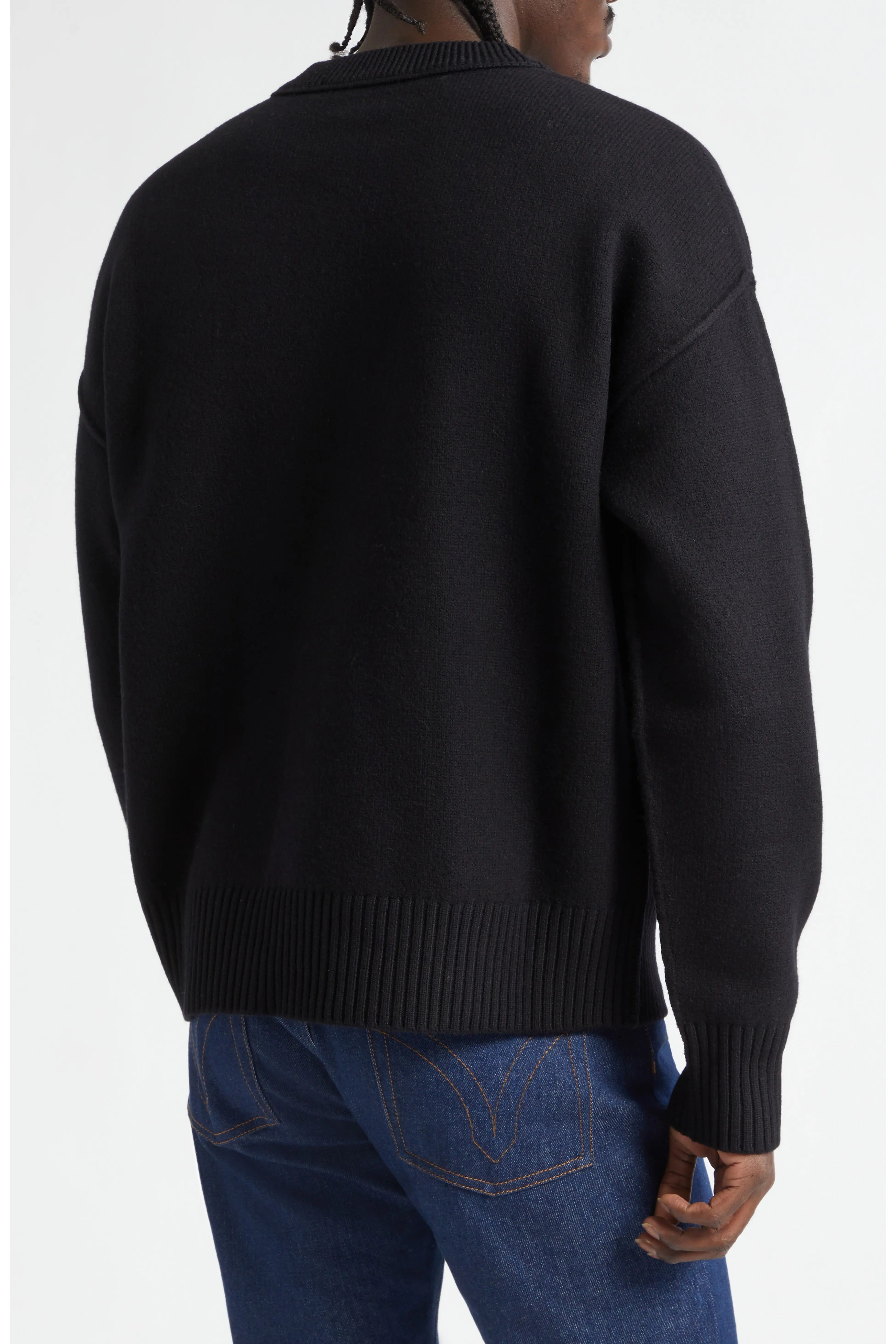 Person wearing a black sweater and blue jeans on a white background