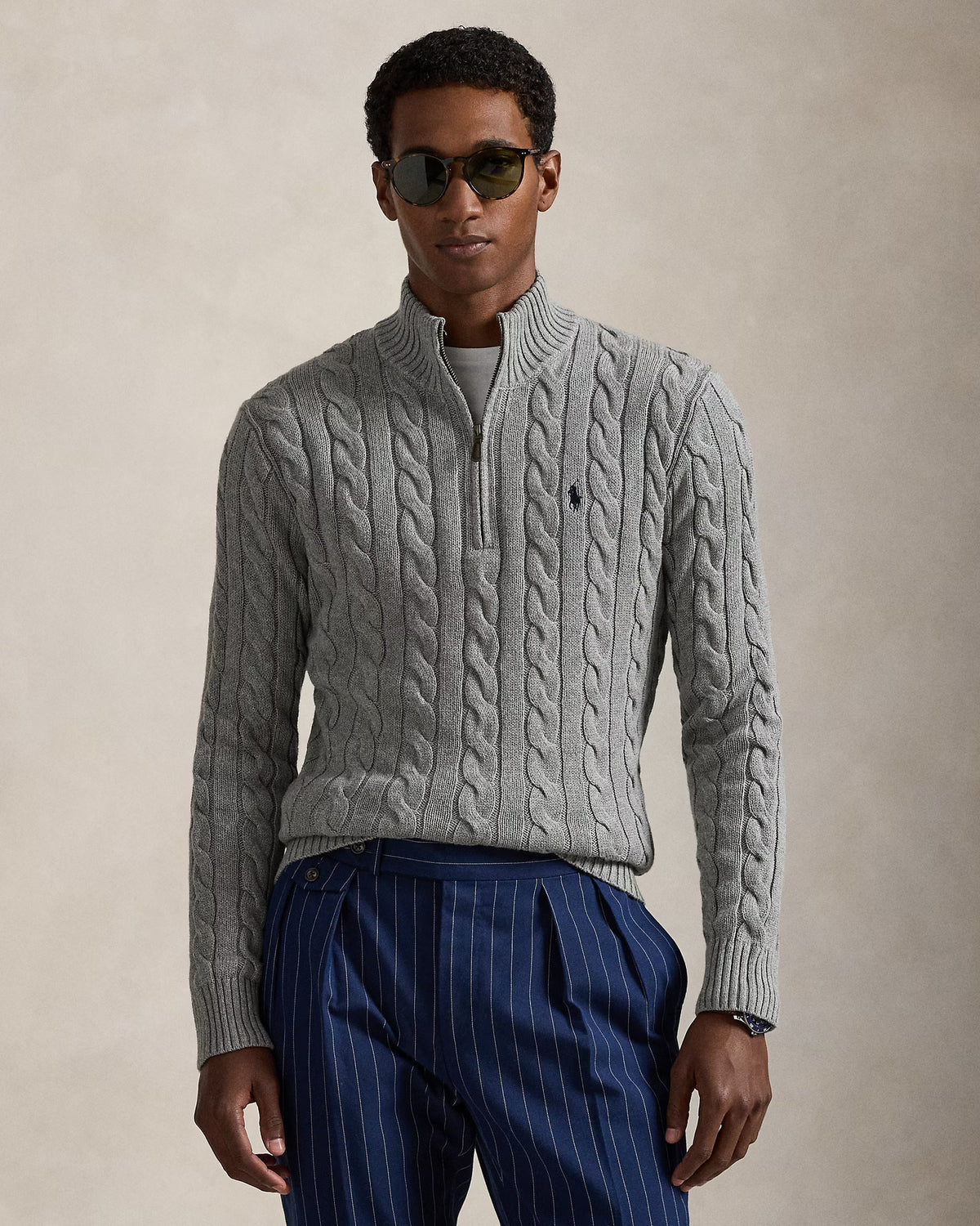 Man wearing a gray cable knit sweater and blue pinstripe pants against a beige background